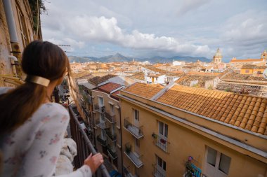 Bir kadın ve beyaz köpeği dar bir balkondan eğilip dramatik bulutlu bir gökyüzünün altında Sicilya 'nın uzak dağlarına ve çatılarına hayran kaldılar.