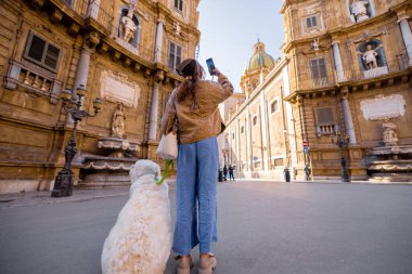 İtalya 'nın Palermo kentindeki Quattro Canti meydanında büyük beyaz köpeğini gezdiren bir kadın. Görüntü yavaş turizmi, evcil hayvanlarla bağlantıyı ve sakin şehir keşfini seyahat için mükemmel kılıyor, evcil hayvan