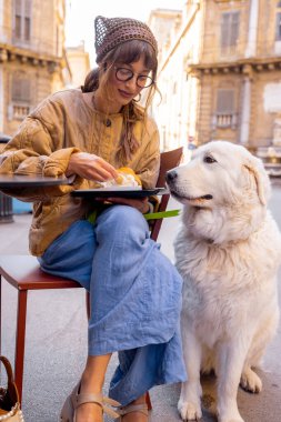 Bir kadın, Palermo 'da bir kafede geleneksel Sicilya dondurmasının tadını çıkarırken köpeğiyle güzel bir anı paylaşıyor. Görüntü sıcaklığı, dostluğu ve otantik yerel yaşam tarzını yakalıyor.