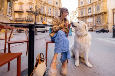 Bir kadın, Palermo 'da bir kafede geleneksel Sicilya dondurmasının tadını çıkarırken köpeğiyle güzel bir anı paylaşıyor. Görüntü sıcaklığı, dostluğu ve otantik yerel yaşam tarzını yakalıyor.