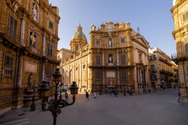 Palermo 'daki Quattro Canti Meydanı' nda altın ışığın barok cepheleri aydınlattığı yerde insanlar geziniyor. Bu fotoğraf, Sicilya 'daki kentsel keşiflerin mimari zarafetini ve cazibesini yansıtıyor.