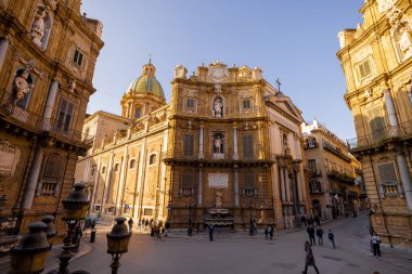 Palermo 'daki Quattro Canti Meydanı' nda altın ışığın barok cepheleri aydınlattığı yerde insanlar geziniyor. Bu fotoğraf, Sicilya 'daki kentsel keşiflerin mimari zarafetini ve cazibesini yansıtıyor.