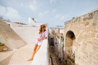 İtalya 'nın güneyindeki sessiz bir çatıda çıplak ayakla dikilen bir kadın. Etrafı güneşli taş duvarlar ve kırsal mimari ile çevrili. Yavaş köy yaşamının huzurunu kucaklıyor.