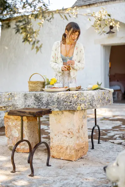 Bir kadın, Puglia 'da bir trullo' nun önündeki taştan bir masada Akdeniz yemeği hazırlıyor. Görüntü, yaşam tarzı ve markalaşma için doğal yaşam ve yavaş besin kavramlarını yakalıyor.