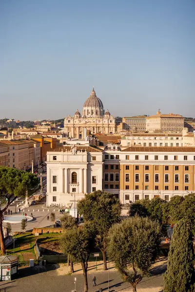 Castel Sant Angelo 'dan Vatikan Şehri ve St. Peters Bazilikası üzerinde geniş çaplı bir manzara, tarihi binalar ve Roma çam ağaçlarıyla çevrili Via della Conciliazione' nin planını ele geçiriyor.