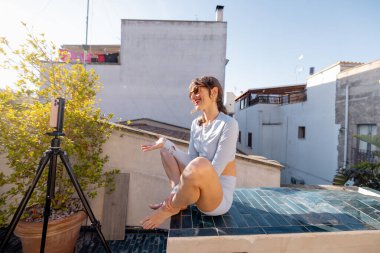 Neşeli bir kadın kendini güneşin altındaki bir çatıda kaydediyor. Etkilenen yaşam tarzı, dijital göçebeler, uzaktan çalışma veya sosyal medya pazarlaması gibi konular için harika