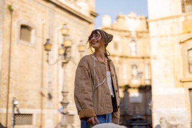 Bir kadın köpeğiyle sabah yürüyüşü sırasında tarihi mimariye bakarken gülümsüyor. Fotoğraf, hayat tarzı, turizm ve sağlıkta kullanmak için ideal olan bilinçli seyahatin özünü yansıtıyor.