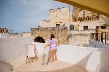 Bir kadın ve beyaz köpeği güneşli bir çatıda sakin bir sabah geçirdiler. Tarihi taş binalar ve güney İtalya 'da bir palmiye ağacı vardı.