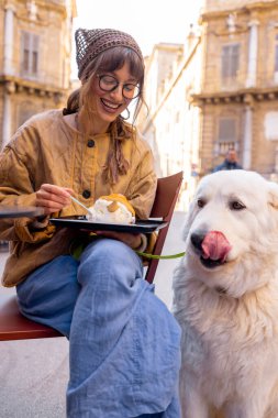 Bir kadın, Palermo 'da bir kafede geleneksel Sicilya dondurmasının tadını çıkarırken köpeğiyle güzel bir anı paylaşıyor. Görüntü sıcaklığı, dostluğu ve otantik yerel yaşam tarzını yakalıyor.