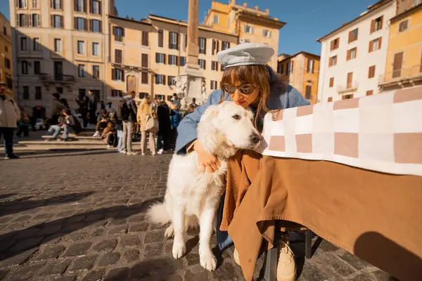 Mavi paltolu bir kadın, Roma meydanındaki bir kafede beyaz köpeğini kucaklıyor. Roma 'nın kalbinde huzurlu bir sevgi anı yakalıyor.