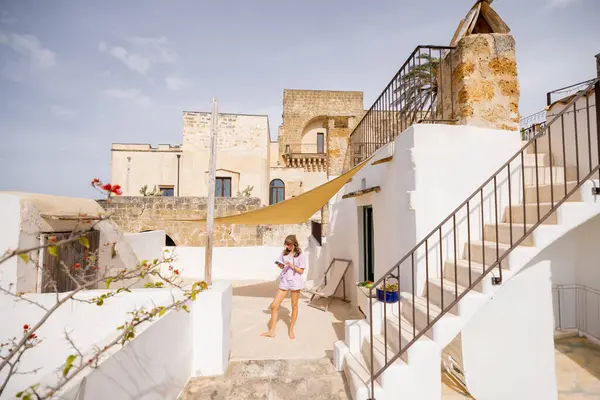 Çatı katındaki terasta bir kitapla rahatlayan, yelken tepe örtüsüyle gölgelenen, beyazlatılmış duvarlar ve Akdeniz mimarisi yaz kaçışıyla çevrili bir kadın.