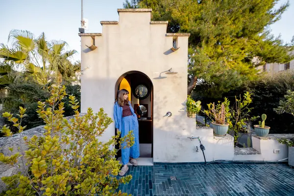 Akdeniz 'de yemyeşil ve seramik ekicilerle çevrili, taştan bir çatı duşunun altında altın saatin tadını çıkaran gevşek bir kadın.