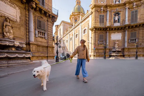 İtalya 'nın Palermo kentindeki Quattro Canti meydanında büyük beyaz köpeğini gezdiren bir kadın. Görüntü yavaş turizmi, evcil hayvanlarla bağlantıyı ve sakin şehir keşfini seyahat için mükemmel kılıyor, evcil hayvan