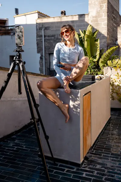 Neşeli bir kadın kendini güneşin altındaki bir çatıda kaydediyor. Etkilenen yaşam tarzı, dijital göçebeler, uzaktan çalışma veya sosyal medya pazarlaması gibi konular için harika