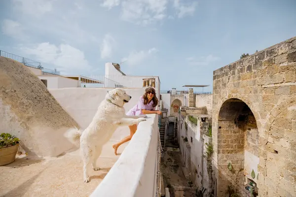 Bir kadın ve onun büyük beyaz köpeği çatıdaki çıkıntıdan eğilip aşağıdaki tarihi İtalyan caddesine bakıyorlar. Güneşli bir köyde huzurlu bir bağ anı