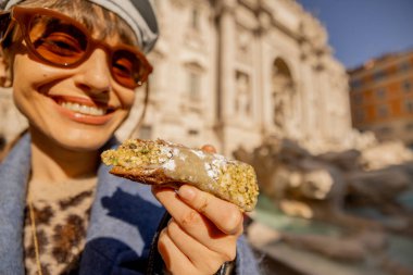Mavi ceketli neşeli bir kadın Roma 'daki Trevi Çeşmesi' nin önünde geleneksel bir cannolo yiyor. İtalya 'nın lezzet ve güneşini kucaklıyor.