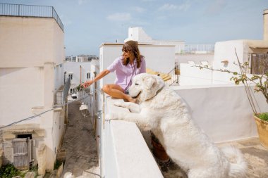 Kadın ve büyük beyaz köpeği güney İtalya 'da güneşli bir çatı terasında sabahın tadını çıkarıyorlar. Neşeli ve sakin seyahat sahnesi Bağlantı ve özgürlük dolu