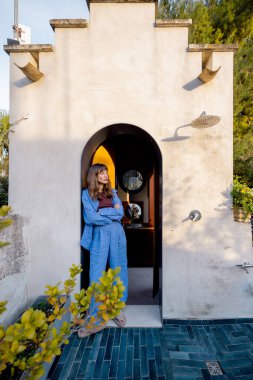 Akdeniz 'de yemyeşil ve seramik ekicilerle çevrili, taştan bir çatı duşunun altında altın saatin tadını çıkaran gevşek bir kadın.