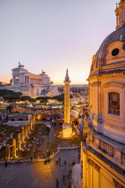 Günbatımında parlayan tarihi bir kubbe ve antik Roma kalıntılarının manzarası. İkonik Altare della Patria, Roma akşam siluetinin üzerinde yükseliyor.
