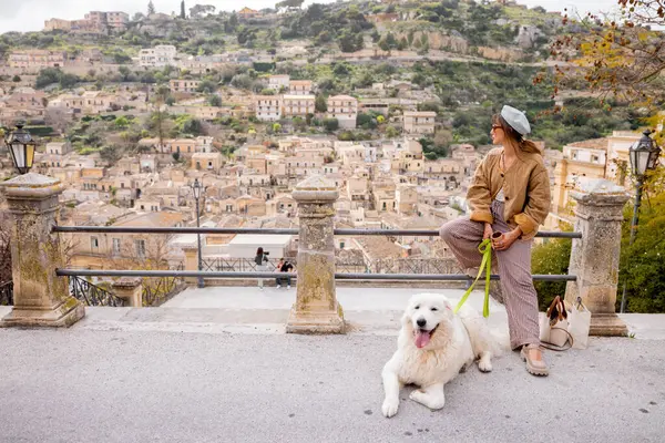 Büyük beyaz köpekli kadın, Sicilya, Modica üzerindeki panoramik manzaranın tadını çıkarıyor. Terracotta çatıları ve barok mimari ile çevrili mükemmel bir bağlantı, huzur ve yavaş seyahat anı.