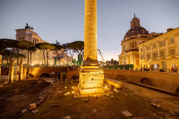 Roma 'nın ikonik Trajans Sütunu ve Altare della Patria' nın akşam manzarası, alacakaranlık gökyüzüne karşı aydınlandı, harabeler, kiliseler ve kaldırım taşı sokaklarla çevrili.