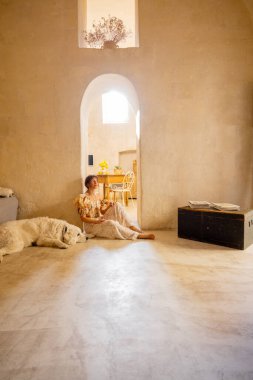 Bir kadın ve köpeği Matera 'da geleneksel bir taş evin serin zemininde dinleniyor. Bu görüntü konforu, dostluğu ve yaşam tarzı ya da refah kullanımı için yavaş iç mekanların güzelliğini yansıtır.