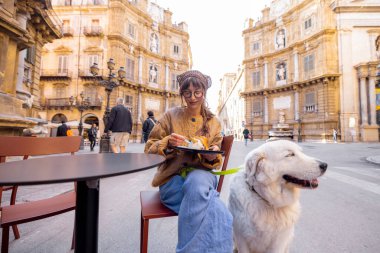Bir kadın, Palermo 'da bir kafede geleneksel Sicilya dondurmasının tadını çıkarırken köpeğiyle güzel bir anı paylaşıyor. Görüntü sıcaklığı, dostluğu ve otantik yerel yaşam tarzını yakalıyor.