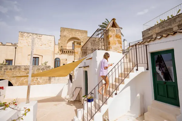Pastel giysili bir kadın, güneşle yıkanmış taş duvarlar ve Akdeniz mimarisi ile çevrili çatıdaki merdivenleri tırmanıyor büyüleyici bir İtalyan kasabasında sakin bir an.
