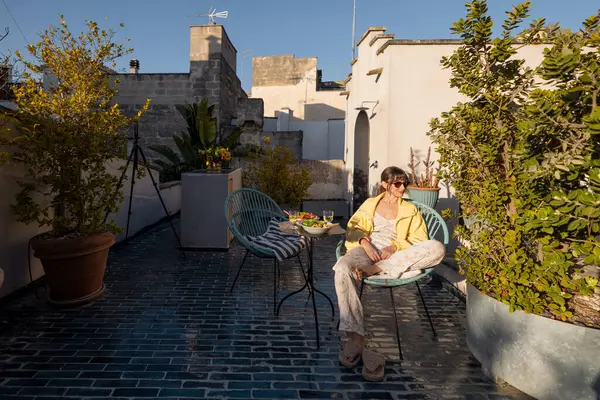 Bir kadın güneşli bir çatıda şarap ve taze salatayla rahatlar. Resim yavaş yaşam, seyahat, konukseverlik ve sağlık yaşam tarzı içeriği için idealdir.