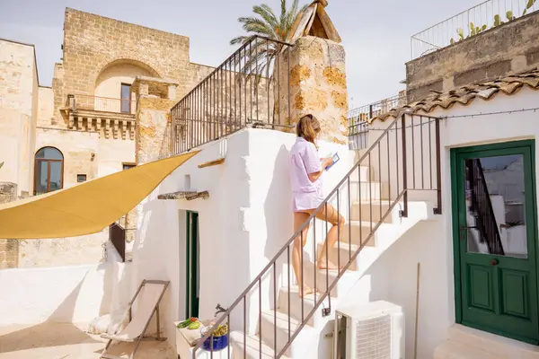 Pastel giysili bir kadın, güneşle yıkanmış taş duvarlar ve Akdeniz mimarisi ile çevrili çatıdaki merdivenleri tırmanıyor büyüleyici bir İtalyan kasabasında sakin bir an.