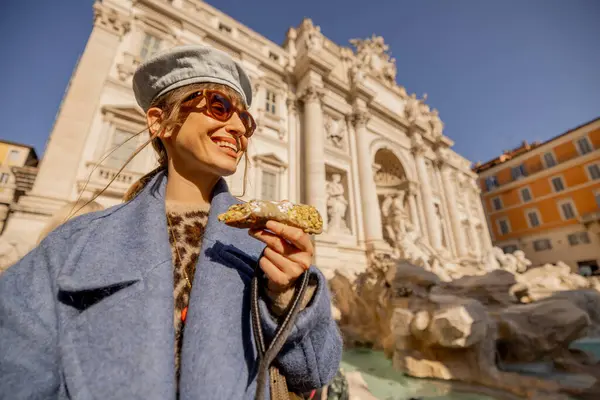 Mavi ceketli neşeli bir kadın Roma 'daki Trevi Çeşmesi' nin önünde geleneksel bir cannolo yiyor. İtalya 'nın lezzet ve güneşini kucaklıyor.