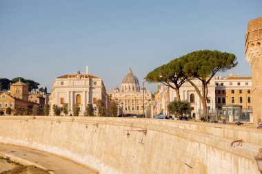 Roma sokaklarında yükselen Aziz Peters Bazilikası manzarası. Önünde taş duvarlar ve çam ağaçları var. Seyahat, yazı işleri veya turizm görselleri için klasik bir Roma perspektifi