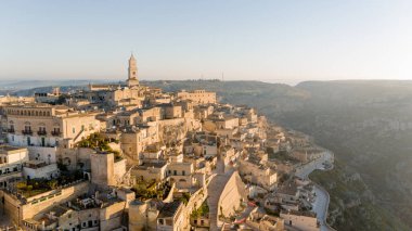 Matera, İtalya 'nın havadan görünüşü, altın sabah ışığıyla yıkanmış. Kanyon üzerinde yükselen ikonik taş evler ve katedral kulesi UNESCO tarafından listelenmiş bu tarihi harikayı gözler önüne seriyor.