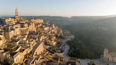 Matera, İtalya 'nın havadan görünüşü, altın sabah ışığıyla yıkanmış. Kanyon üzerinde yükselen ikonik taş evler ve katedral kulesi UNESCO tarafından listelenmiş bu tarihi harikayı gözler önüne seriyor.