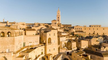 Matera, İtalya 'nın havadan görünüşü, altın sabah ışığıyla yıkanmış. Kanyon üzerinde yükselen ikonik taş evler ve katedral kulesi UNESCO tarafından listelenmiş bu tarihi harikayı gözler önüne seriyor.