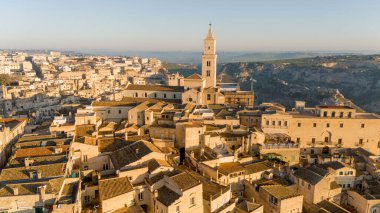 Matera, İtalya 'nın havadan görünüşü, altın sabah ışığıyla yıkanmış. Kanyon üzerinde yükselen ikonik taş evler ve katedral kulesi UNESCO tarafından listelenmiş bu tarihi harikayı gözler önüne seriyor.
