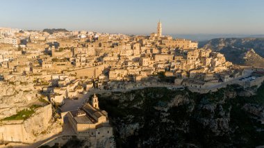 Matera, İtalya 'nın havadan görünüşü, altın sabah ışığıyla yıkanmış. Kanyon üzerinde yükselen ikonik taş evler ve katedral kulesi UNESCO tarafından listelenmiş bu tarihi harikayı gözler önüne seriyor.