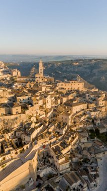 Matera, İtalya 'nın havadan görünüşü, altın sabah ışığıyla yıkanmış. Kanyon üzerinde yükselen ikonik taş evler ve katedral kulesi UNESCO tarafından listelenmiş bu tarihi harikayı gözler önüne seriyor.