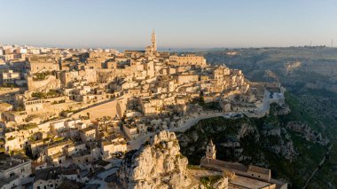 Matera, İtalya 'nın havadan görünüşü, altın sabah ışığıyla yıkanmış. Kanyon üzerinde yükselen ikonik taş evler ve katedral kulesi UNESCO tarafından listelenmiş bu tarihi harikayı gözler önüne seriyor.