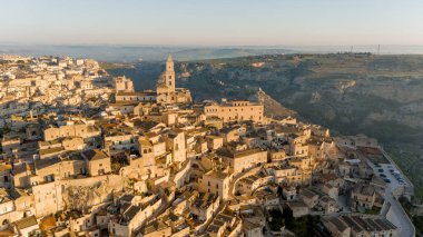 Matera, İtalya 'nın havadan görünüşü, altın sabah ışığıyla yıkanmış. Kanyon üzerinde yükselen ikonik taş evler ve katedral kulesi UNESCO tarafından listelenmiş bu tarihi harikayı gözler önüne seriyor.