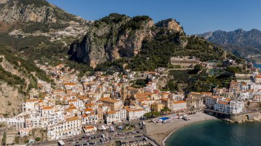 Dik uçurumlar ve Akdeniz arasında yer alan Amalfi adlı pitoresk kasabanın insansız hava aracı görüntüsü. Tarihi cazibesi, kumlu plajı ve teraslı yamaçları olan bir sahil mücevheri.