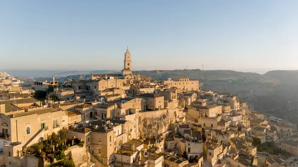Matera, İtalya 'nın havadan görünüşü, altın sabah ışığıyla yıkanmış. Kanyon üzerinde yükselen ikonik taş evler ve katedral kulesi UNESCO tarafından listelenmiş bu tarihi harikayı gözler önüne seriyor.