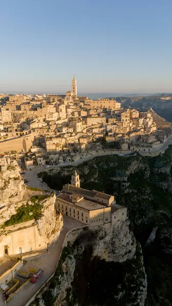 Matera, İtalya 'nın havadan görünüşü, altın sabah ışığıyla yıkanmış. Kanyon üzerinde yükselen ikonik taş evler ve katedral kulesi UNESCO tarafından listelenmiş bu tarihi harikayı gözler önüne seriyor.