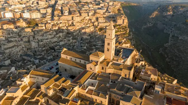 Matera, İtalya 'nın havadan görünüşü, altın sabah ışığıyla yıkanmış. Kanyon üzerinde yükselen ikonik taş evler ve katedral kulesi UNESCO tarafından listelenmiş bu tarihi harikayı gözler önüne seriyor.