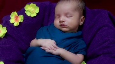Bebek ambalajında uyuyan yeni doğmuş şirin bir bebek. Çiçeklerle süslenmiş. Üst açıdan çekilmiş.