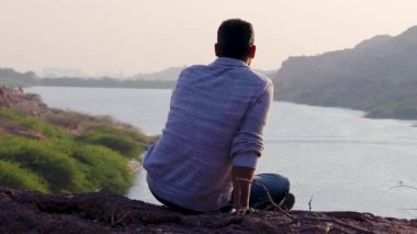 Düz açılı videoyla dağın tepesinde oturan izole genç adam, Hindistan 'daki Kaylana Gölü Jodhpur Rajasthan' da çekildi..