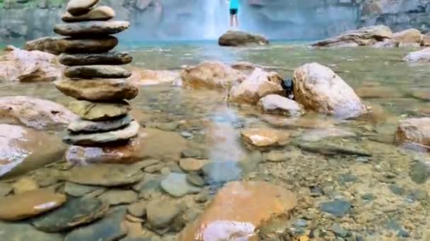 孤立した男が岩の上に座り落石の山から滝が落ちる日のショットでメガラヤで撮影されています — ストック動画