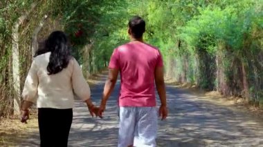 İzole edilmiş asfalt yolda yürüyen genç çift gün içinde düz bir açıdan yemyeşil ağaçla kaplanmış.