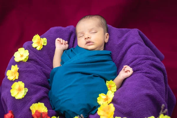Bebek ambalajında uyuyan yeni doğmuş şirin bir bebek. Çiçeklerle süslenmiş. Üst açıdan çekilmiş.