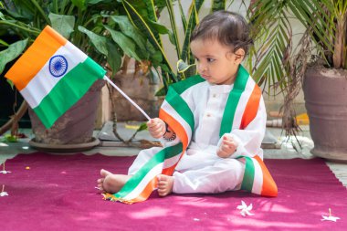 Masum bir yüz ifadesiyle geleneksel giysinin içinde üç renkli Hint bayrağı tutan sevimli çocuk.